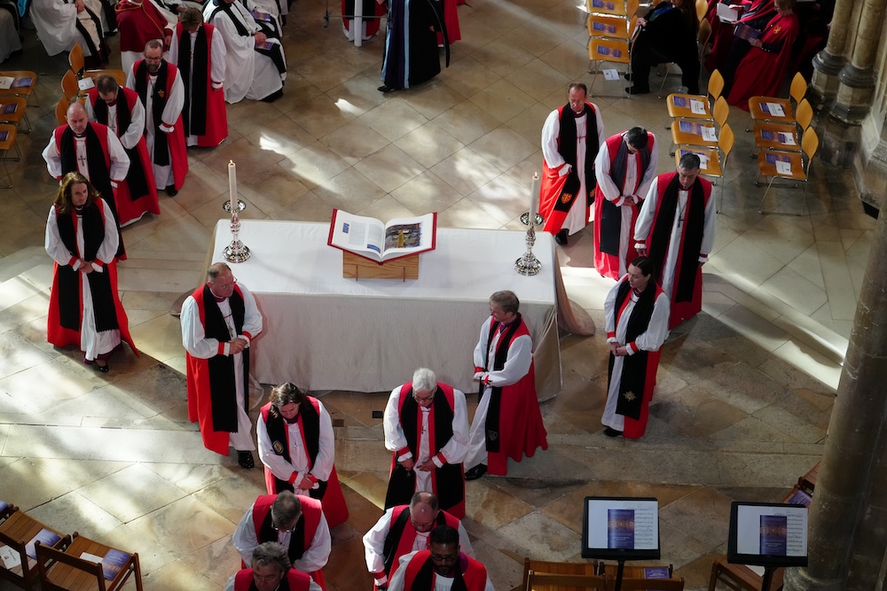 several clergy members surround an open Bible in a sunlit cathedral